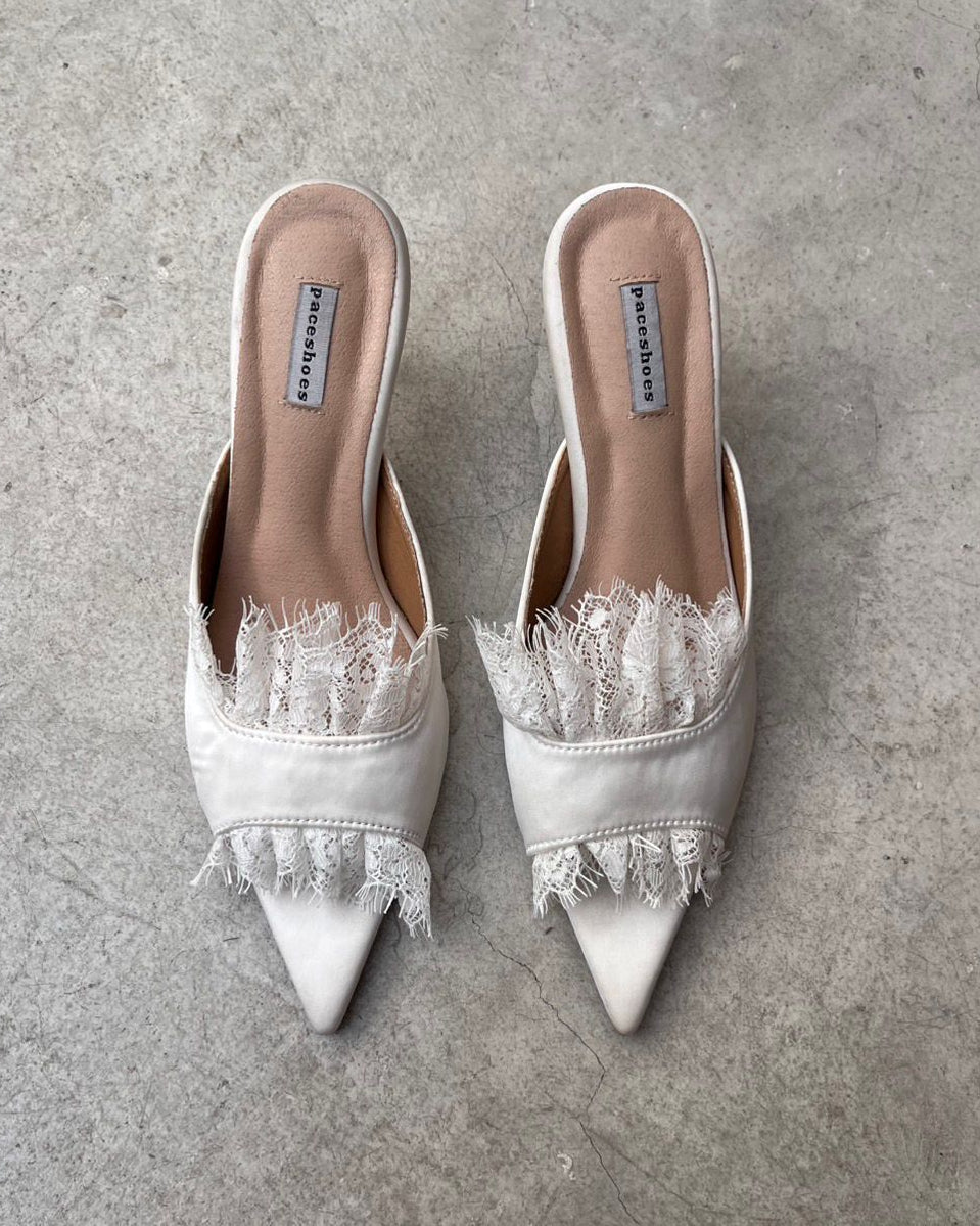 White pointed-toe shoes with lace details on a gray concrete floor